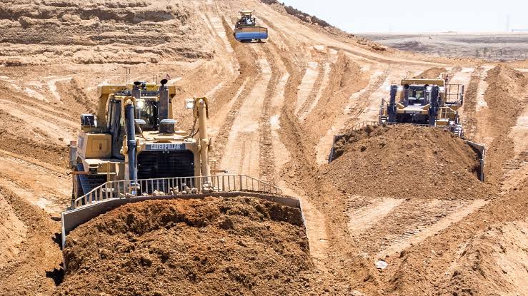 Empty-cab excavator on bare earth with a remote control room, autonomy land grab.